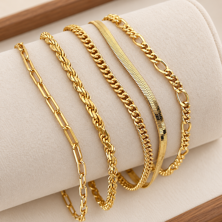 Set de cinco pulseras de cadena doradas, cada una con un eslabón distinto, sobre un soporte de terciopelo crema